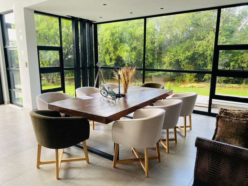 Modern dining area featuring large format floor tiles and expansive black aluminium frame windows offering views of the surrounding garden.