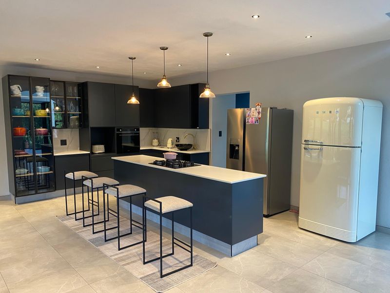 Modern kitchen featuring dark cabinetry, a central island with a gas hob, stone countertops, and high-quality finishes throughout.