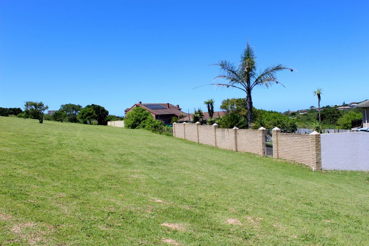 A view of a vacant residential plot featuring a well-maintained brick boundary wall, established greenery, and neighboring properties with solar installations.