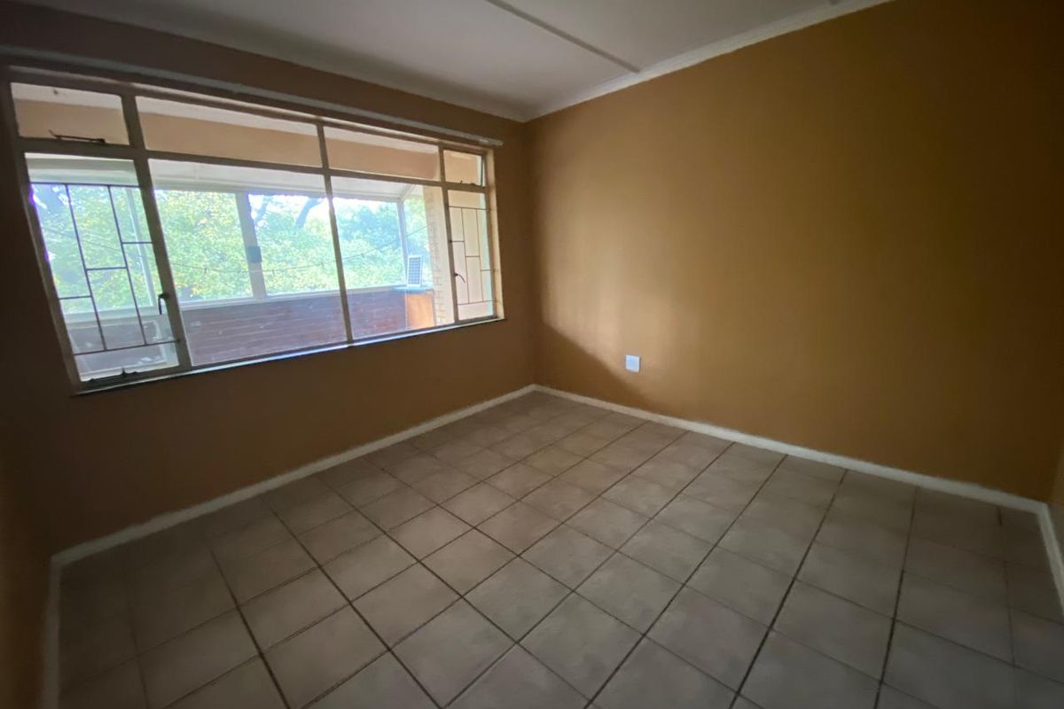 An empty bedroom featuring tiled flooring and a large window with security bars, offering a blank canvas for personalization.