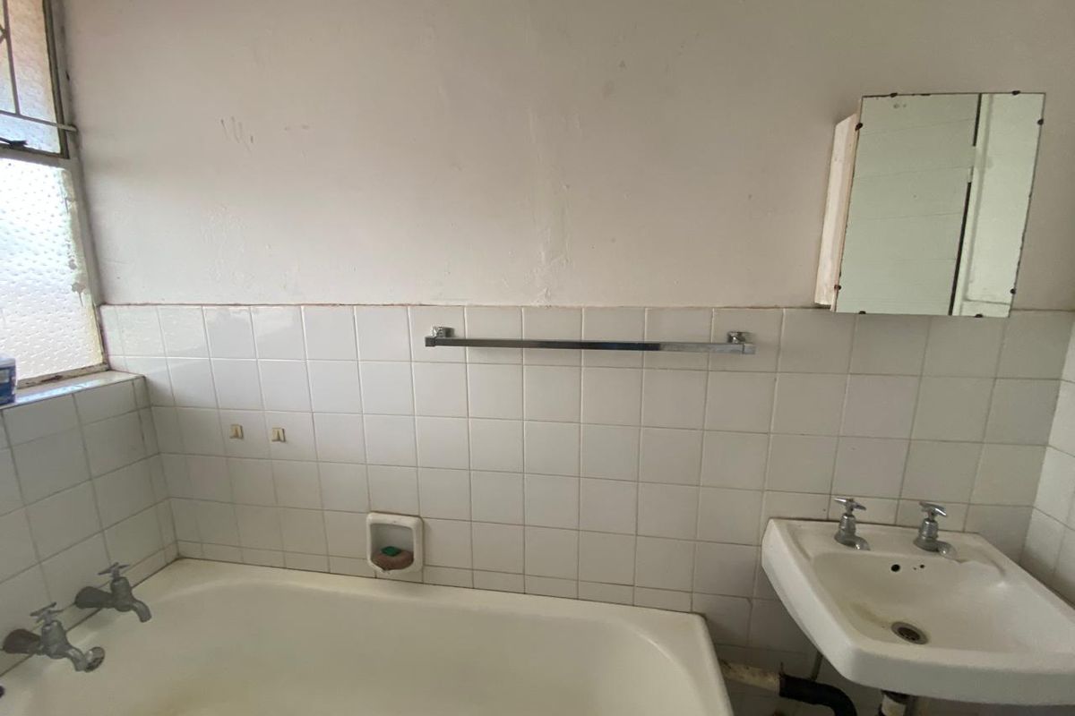 A dated bathroom featuring a standard bathtub, wall-mounted basin, and tiled splashback, requiring renovation to update the finishes and fixtures.