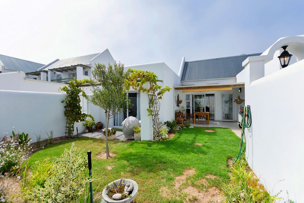 A well-maintained rear garden featuring a lush lawn, paved patio area, and white exterior walls with integrated lighting.