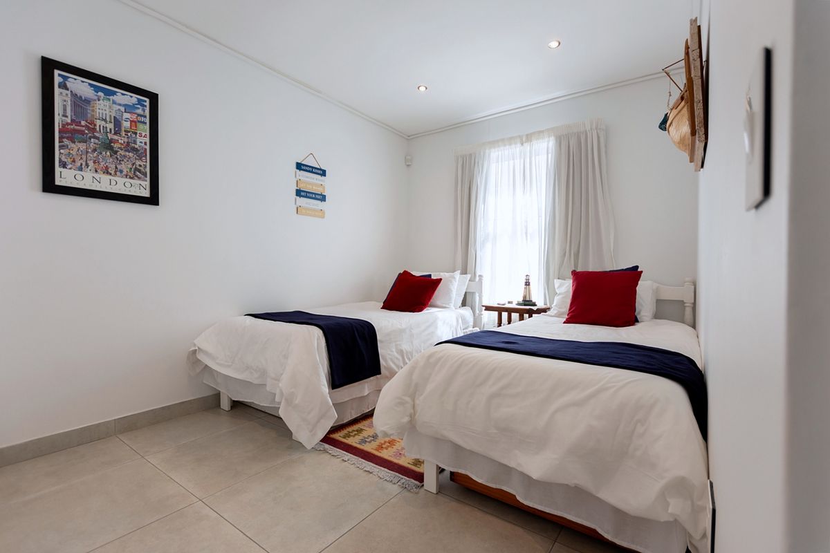 A bright bedroom featuring neutral tiled flooring, recessed ceiling lighting, and a window with curtains.