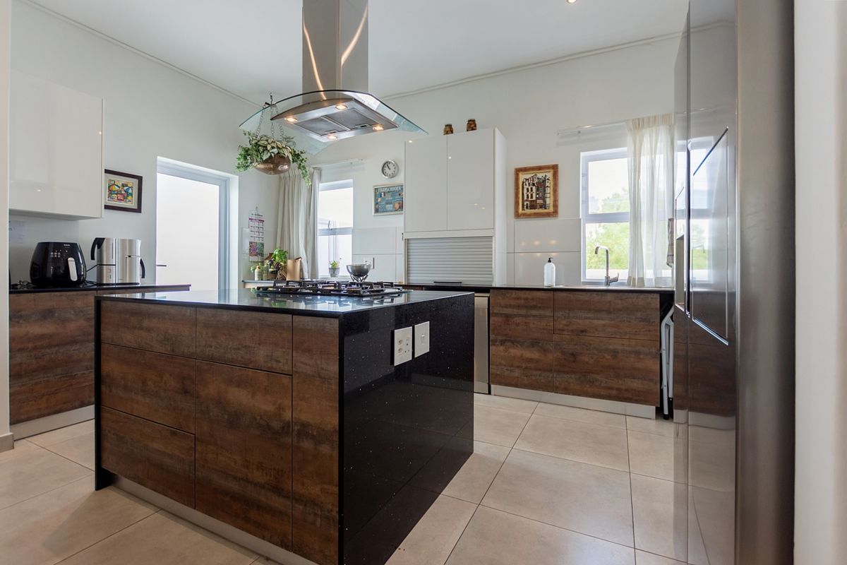 Modern kitchen featuring a central island with a built-in gas hob, stainless steel extractor fan, dark stone countertops, and wood-finish cabinetry.