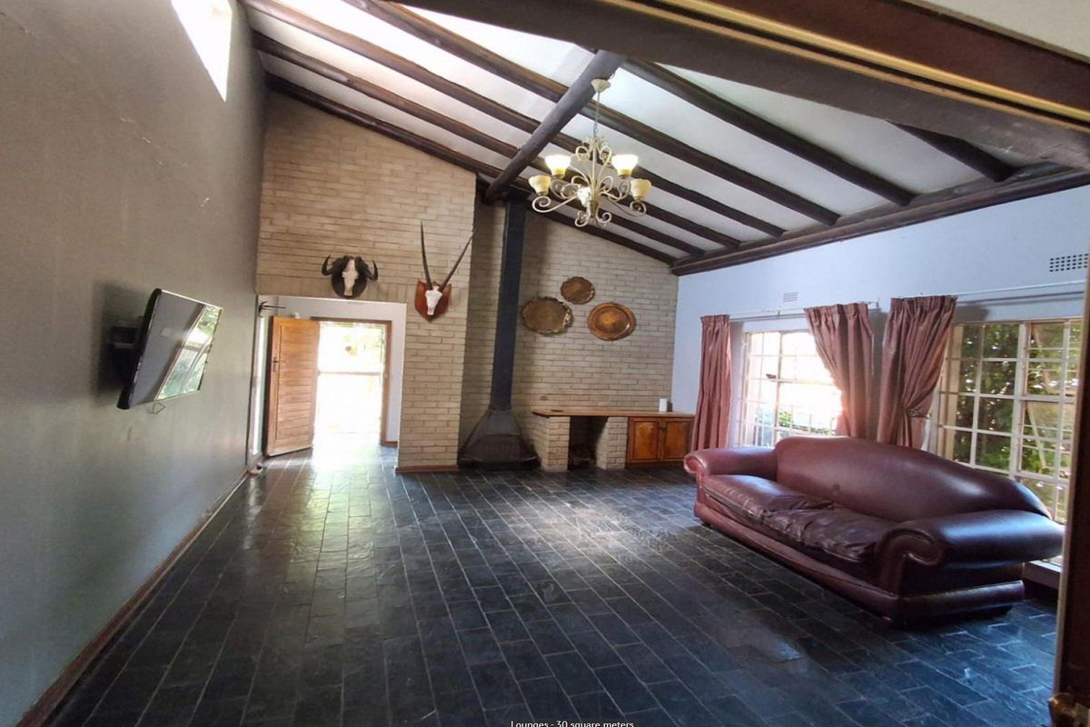 Spacious living room featuring vaulted ceilings with exposed timber beams, a brick fireplace, and dark slate tile flooring.