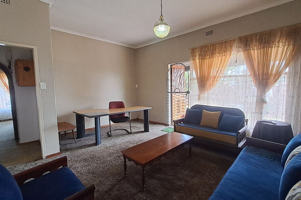 A living room area featuring carpet flooring, a ceiling pendant light, and a security gate leading to the exterior.