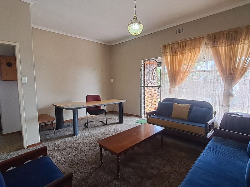 A living room area featuring carpet flooring, a ceiling pendant light, and a security gate leading to the exterior.