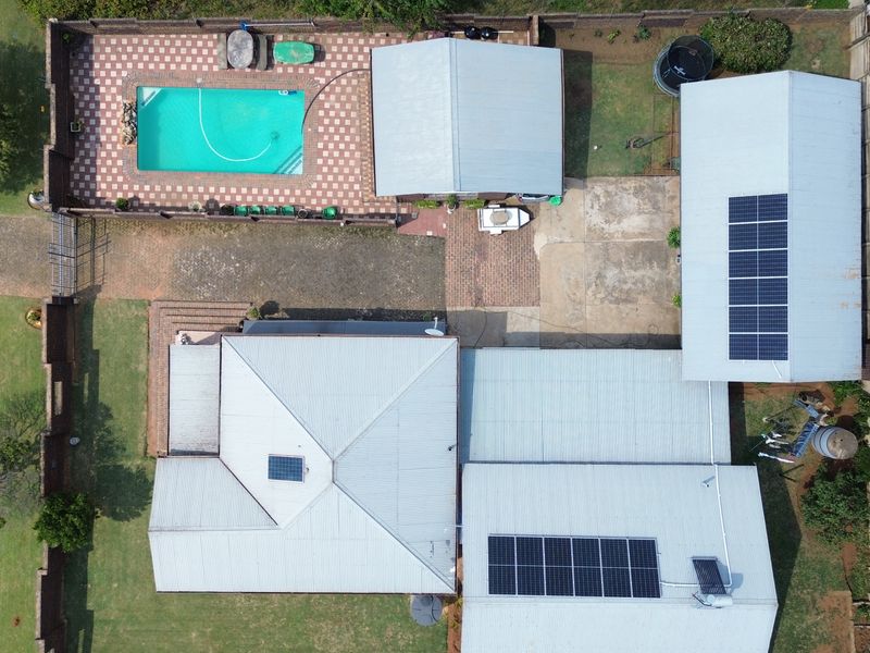 Aerial view of the property featuring a swimming pool, multiple roof structures with solar panel installations, and a paved driveway area.
