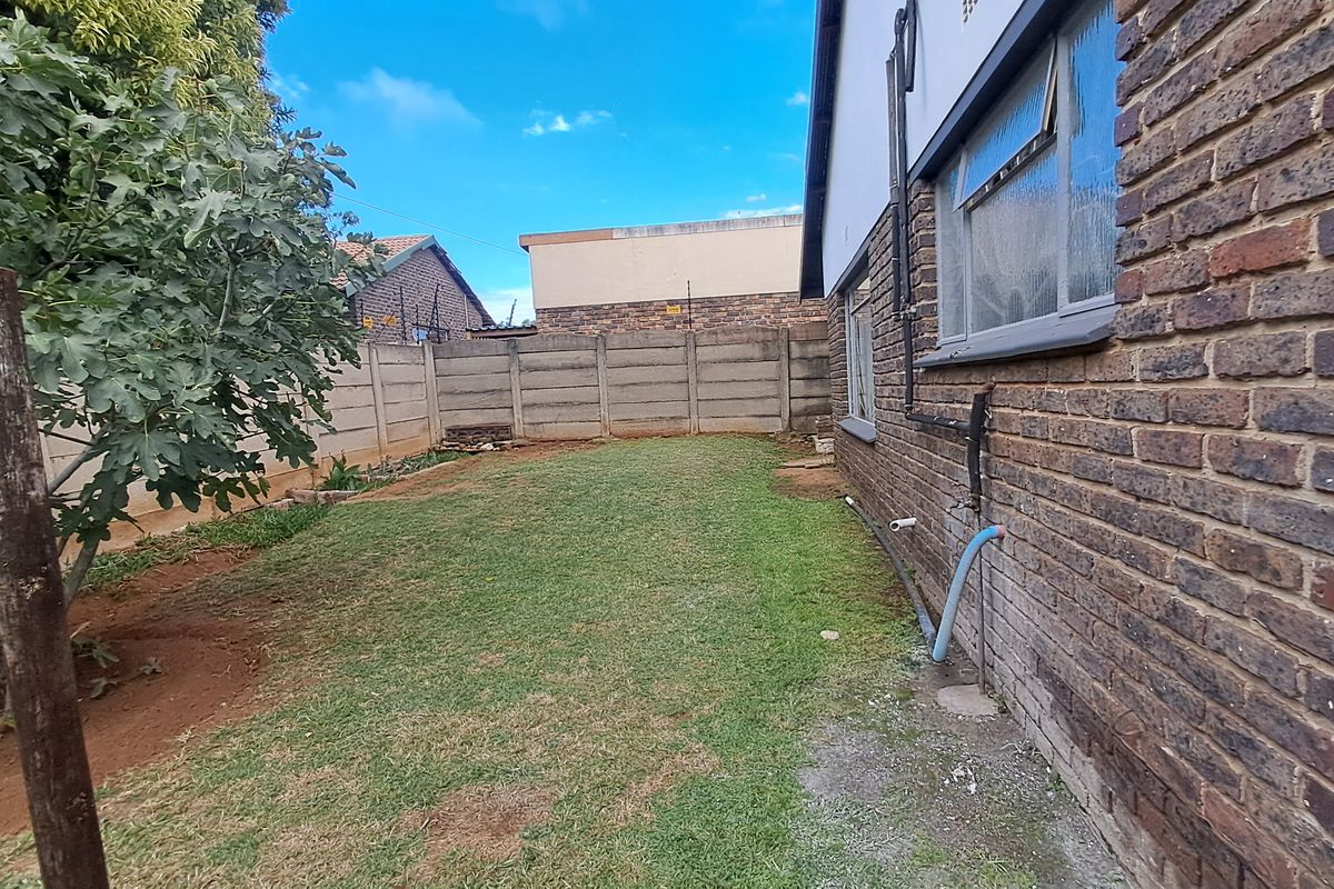 A view of the rear garden featuring a brick exterior wall, precast concrete boundary fencing, and a grass lawn area.
