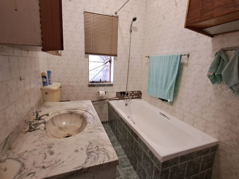 A dated bathroom featuring a marble-effect vanity, inset basin, and a bathtub with tiled surround and wall finishes.