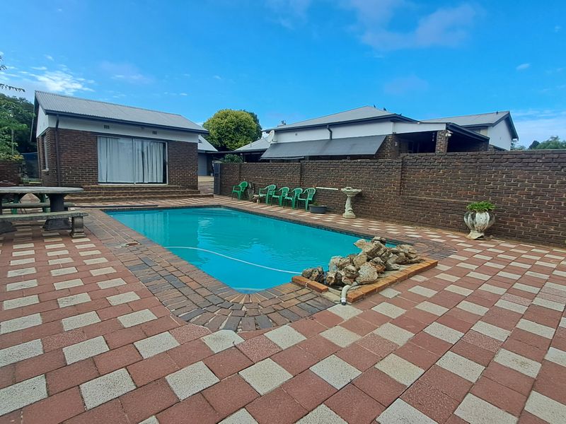 Outdoor pool area featuring a paved patio, brick boundary walls, and access to an adjacent outbuilding with a sliding glass door.