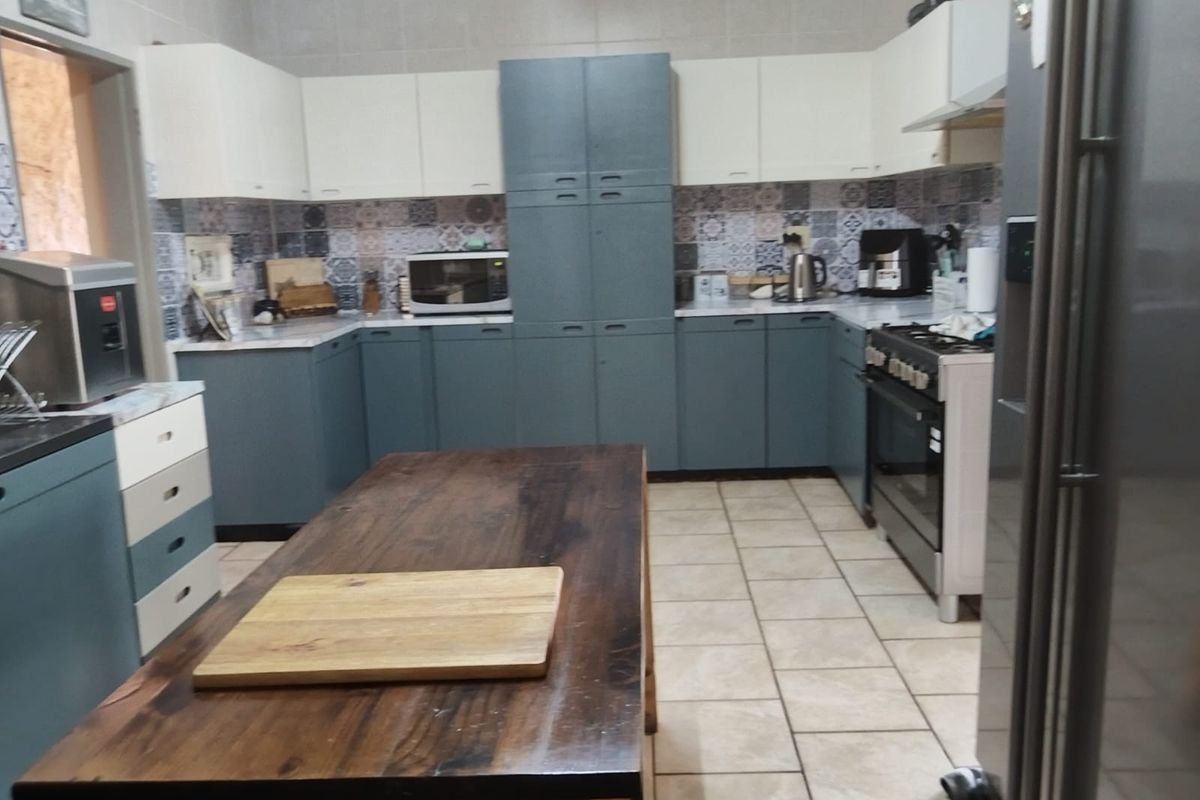 A functional kitchen featuring two-tone cabinetry, patterned tile backsplash, tiled flooring, and a central wooden island workspace.