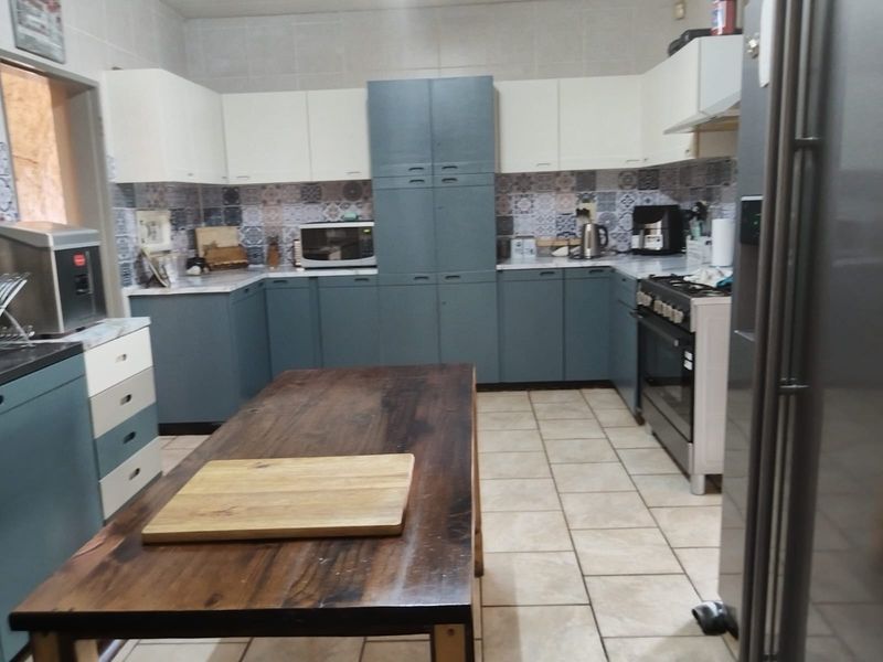 A functional kitchen featuring two-tone cabinetry, patterned tile backsplash, tiled flooring, and a central wooden island workspace.