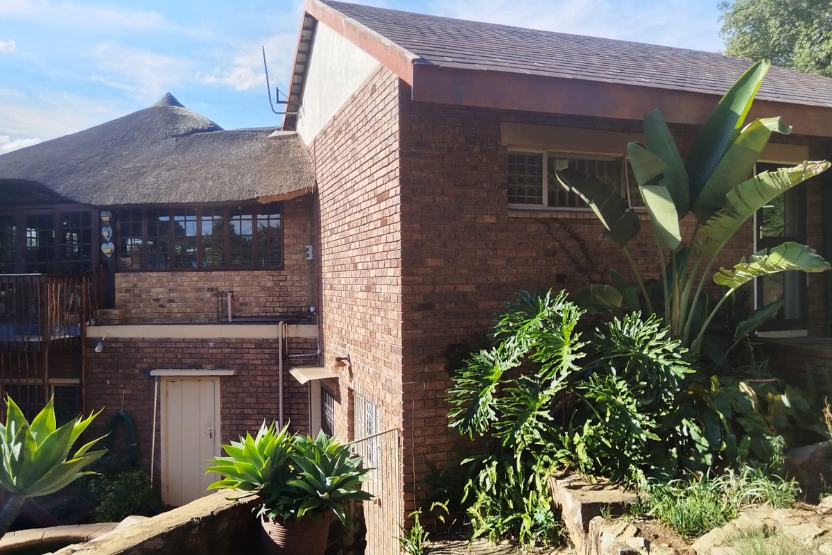 Rear view of a multi-level brick house featuring a combination of thatched and tiled roofing, timber window frames, and a balcony.