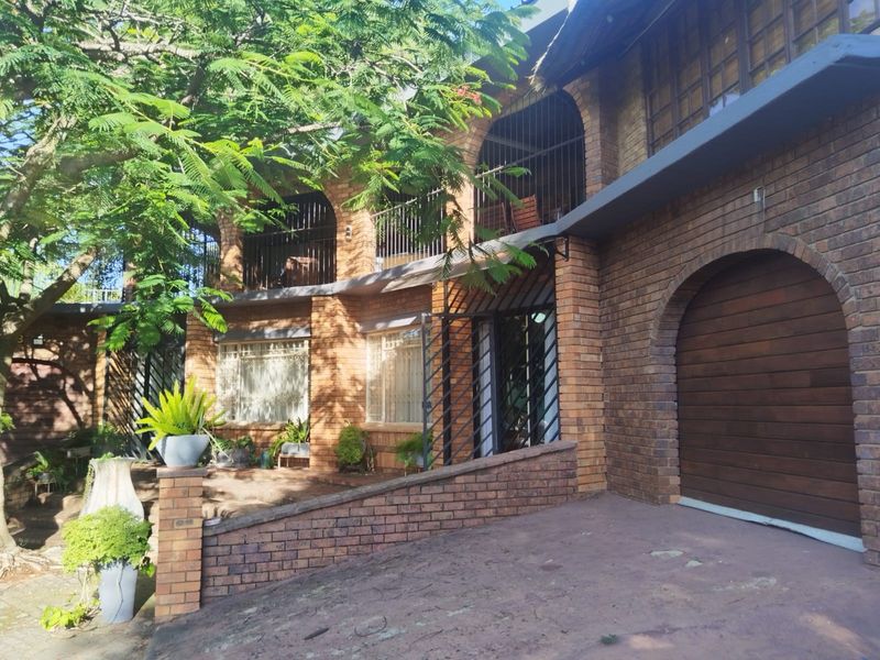 A multi-level face brick house featuring an arched garage door, upper-level balcony with metal railings, and a paved driveway.