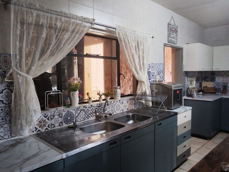 A functional kitchen featuring a double stainless steel sink, patterned tile backsplash, and ample built-in cabinetry with laminate countertops.