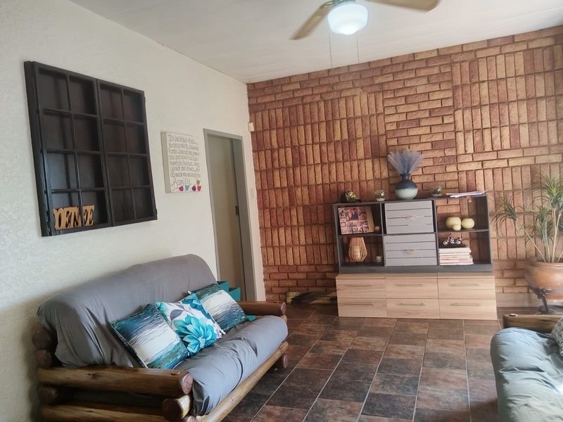 A living room featuring a prominent exposed brick feature wall, tiled flooring, and a ceiling fan, offering a rustic aesthetic.