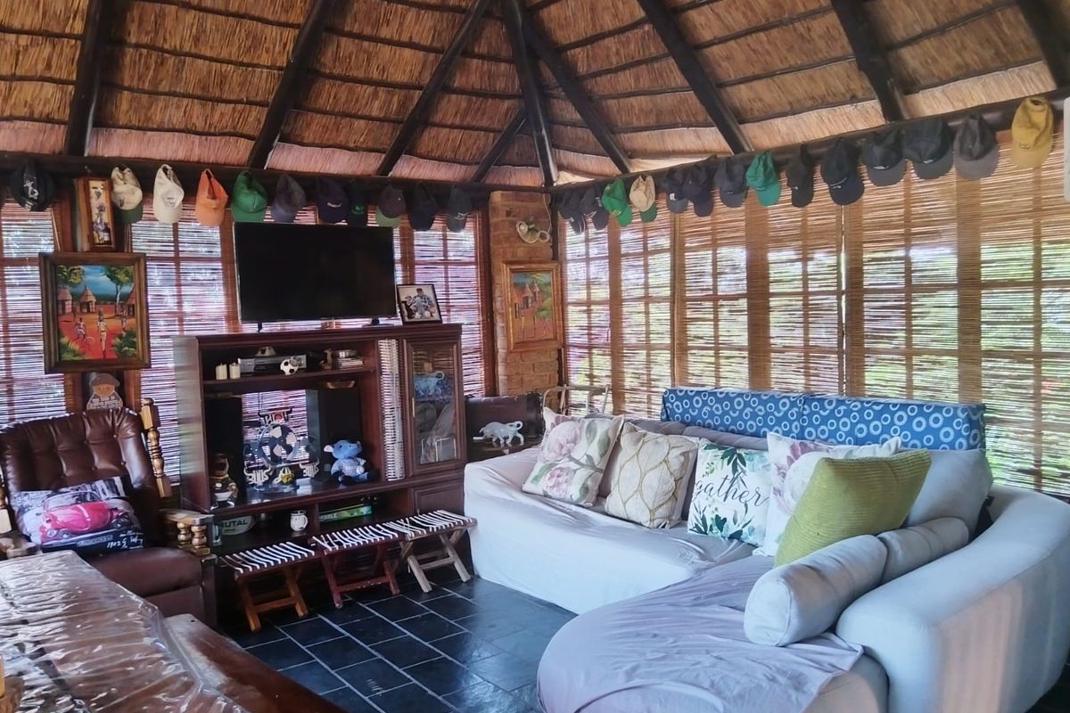 A rustic living area featuring a high vaulted thatched roof with exposed timber rafters, slate tile flooring, and bamboo window blinds.