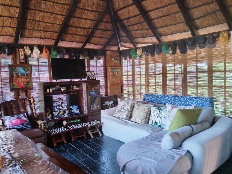 A rustic living area featuring a high vaulted thatched roof with exposed timber rafters, slate tile flooring, and bamboo window blinds.