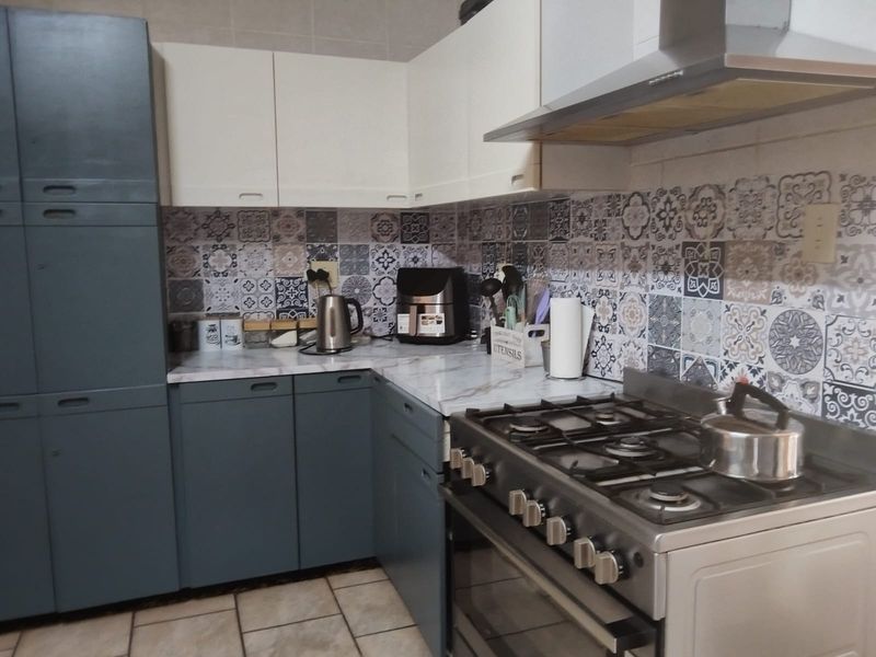 A functional kitchen featuring two-tone cabinetry, a gas stove with an extractor fan, and decorative patterned tile backsplash.