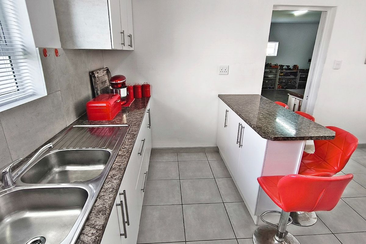 A functional kitchen featuring white cabinetry, granite countertops, a double stainless steel sink, and a breakfast bar island with tiled flooring.