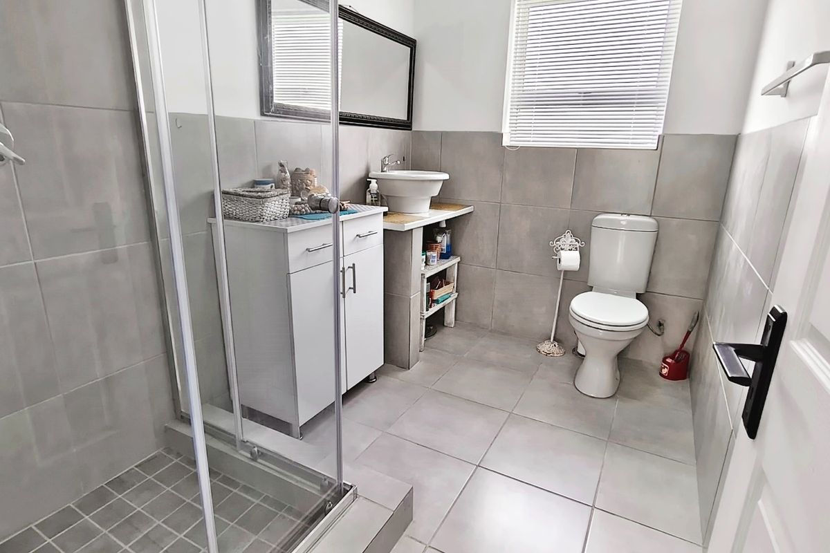 A modern bathroom featuring a glass-enclosed shower, a vessel sink vanity, and neutral floor-to-ceiling tiling.