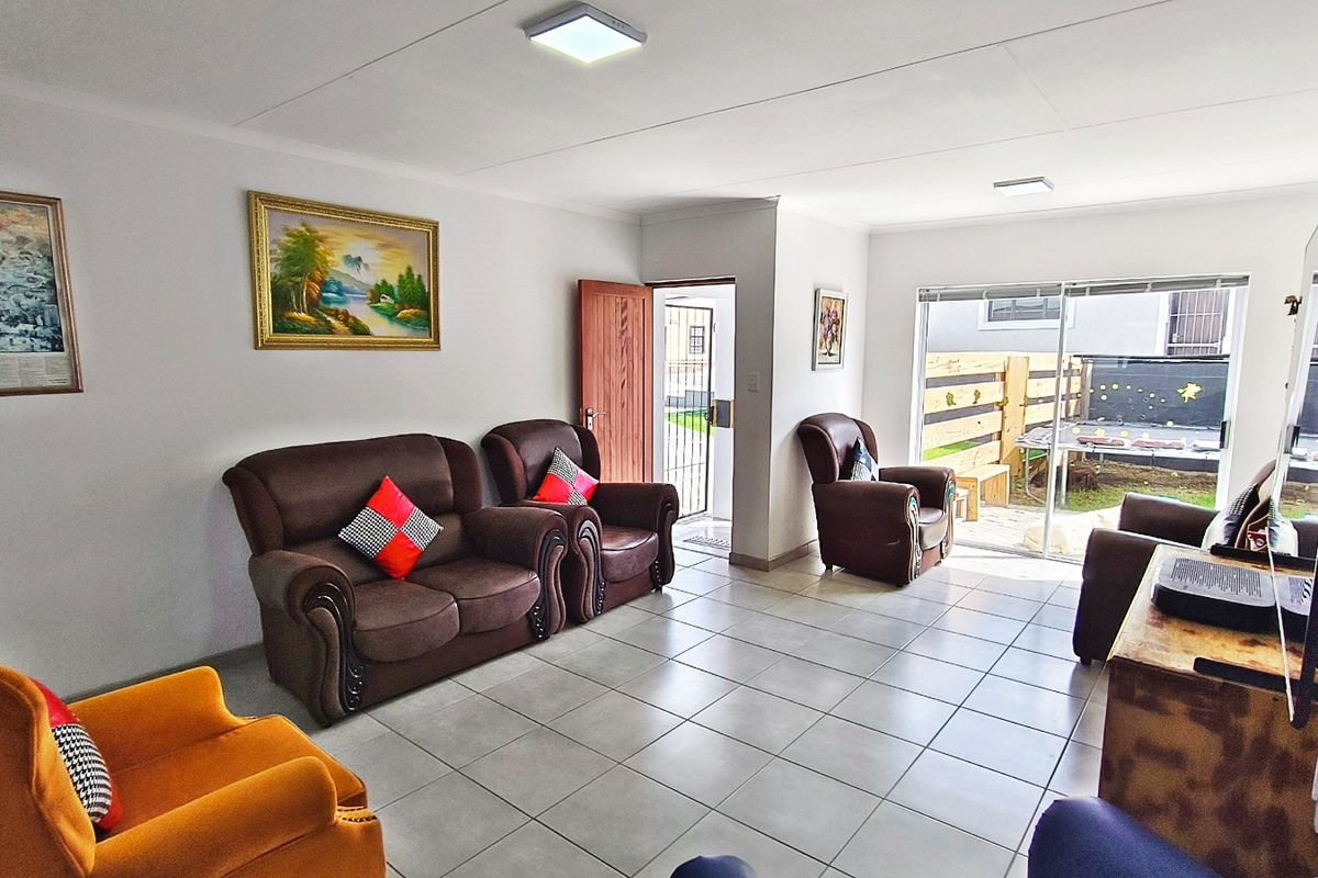 A bright living room featuring neutral floor tiles, sliding glass doors leading to an outdoor area, and a direct entrance door.
