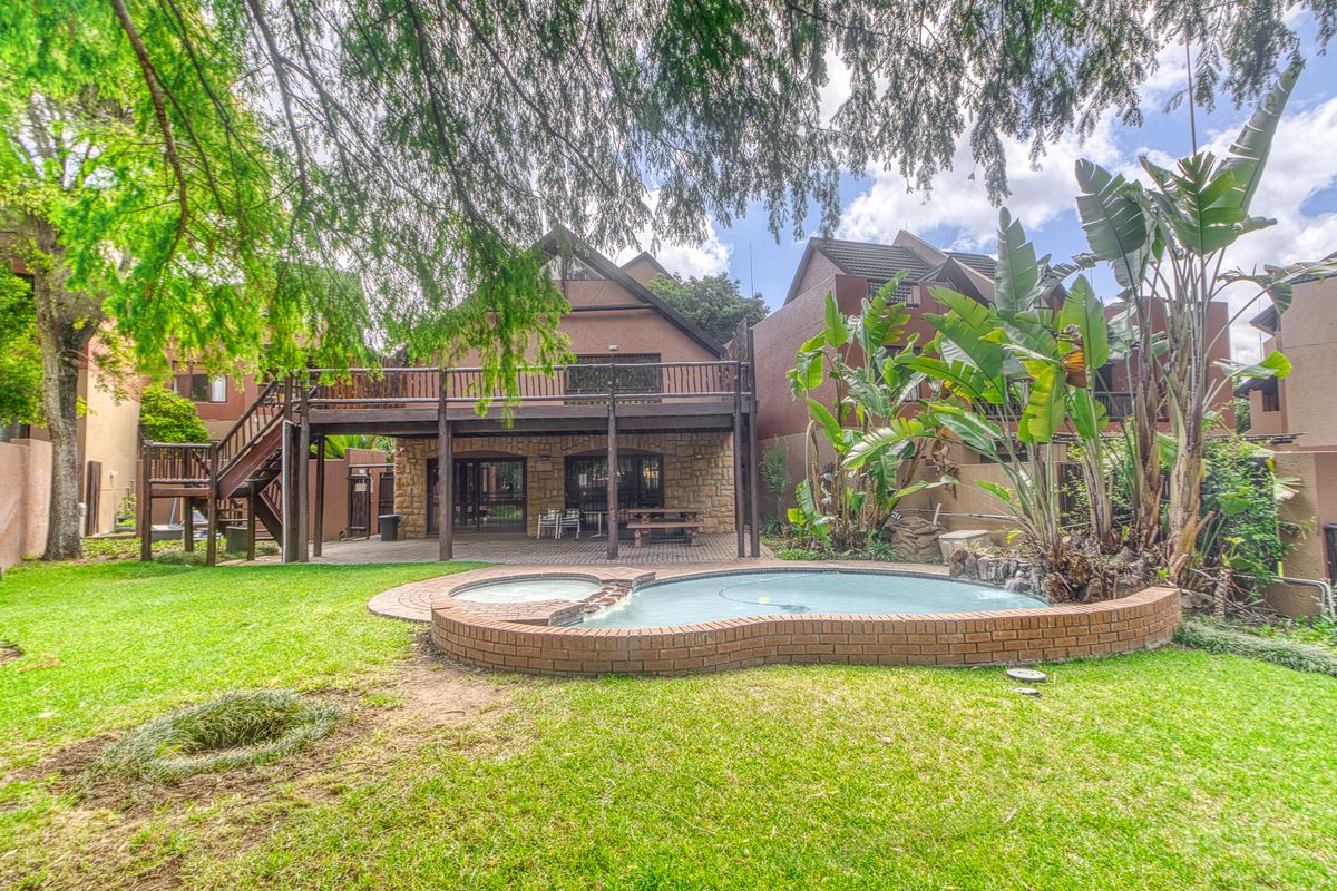 Rear view of the property featuring a private swimming pool, raised wooden deck, and stone-clad lower level with sliding door access to the garden.