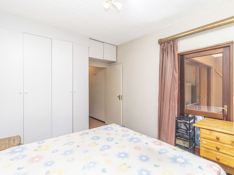 A bedroom featuring built-in cupboards, a wooden window frame, and ceiling panels, offering a functional space with potential for modernization.
