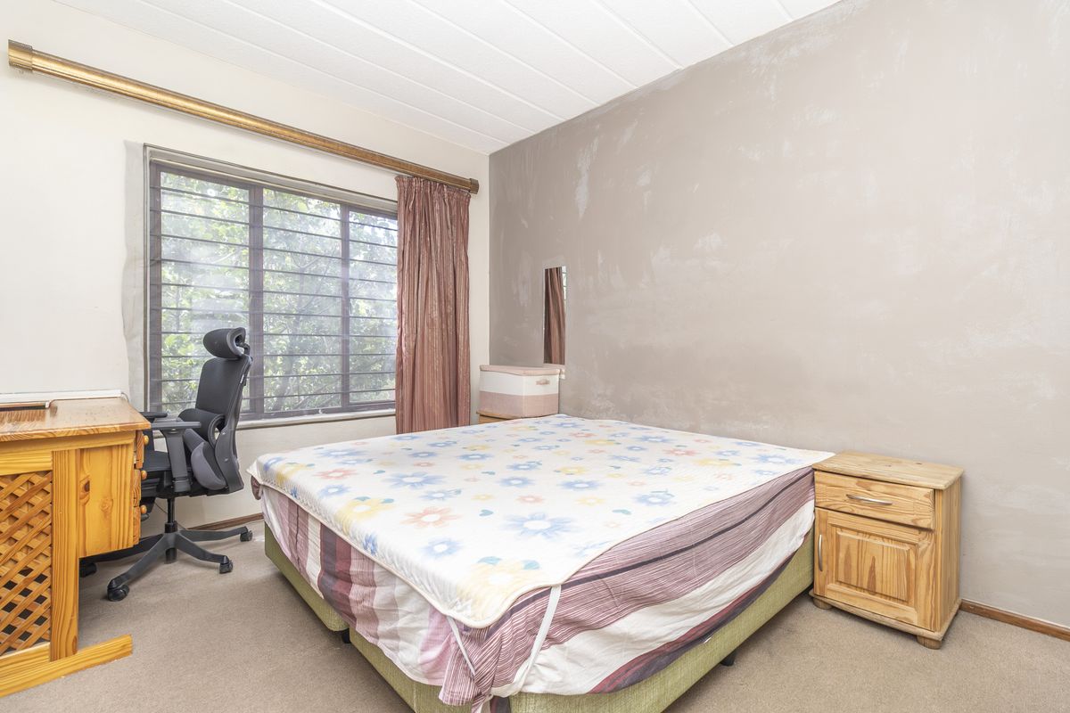 A bedroom featuring carpeted flooring, a window with security bars, and a curtain rail. The walls require cosmetic attention and repainting.
