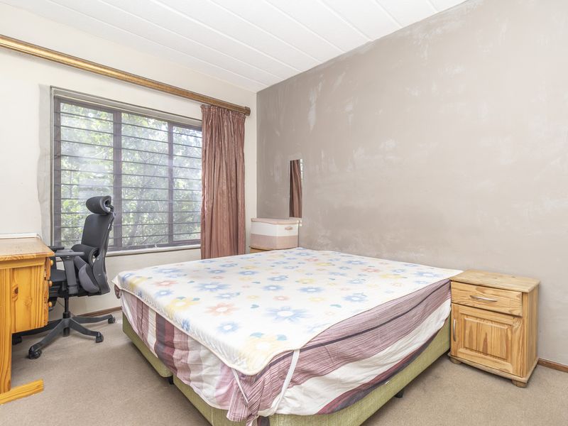 A bedroom featuring carpeted flooring, a window with security bars, and a curtain rail. The walls require cosmetic attention and repainting.