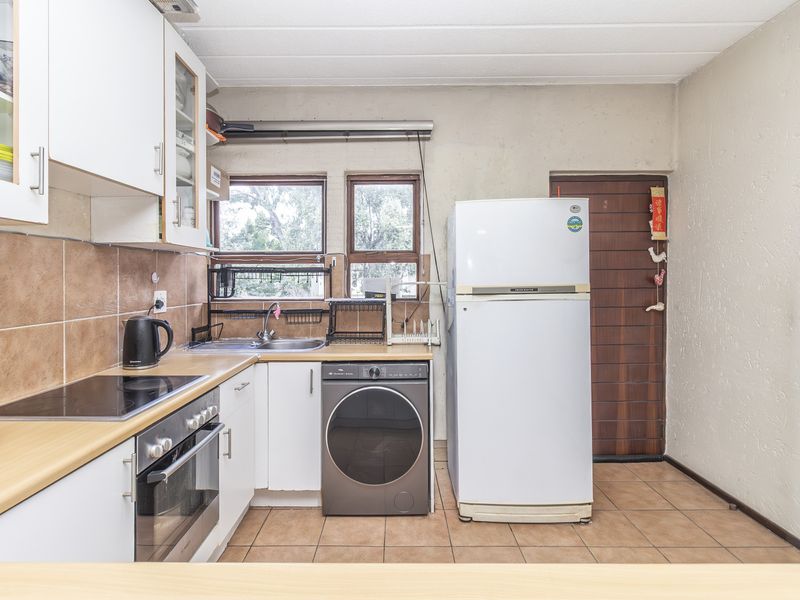 Functional kitchen featuring white cabinetry, laminate countertops, tiled backsplash, built-in oven, and cooktop, with tiled flooring and direct access to an exterior door.