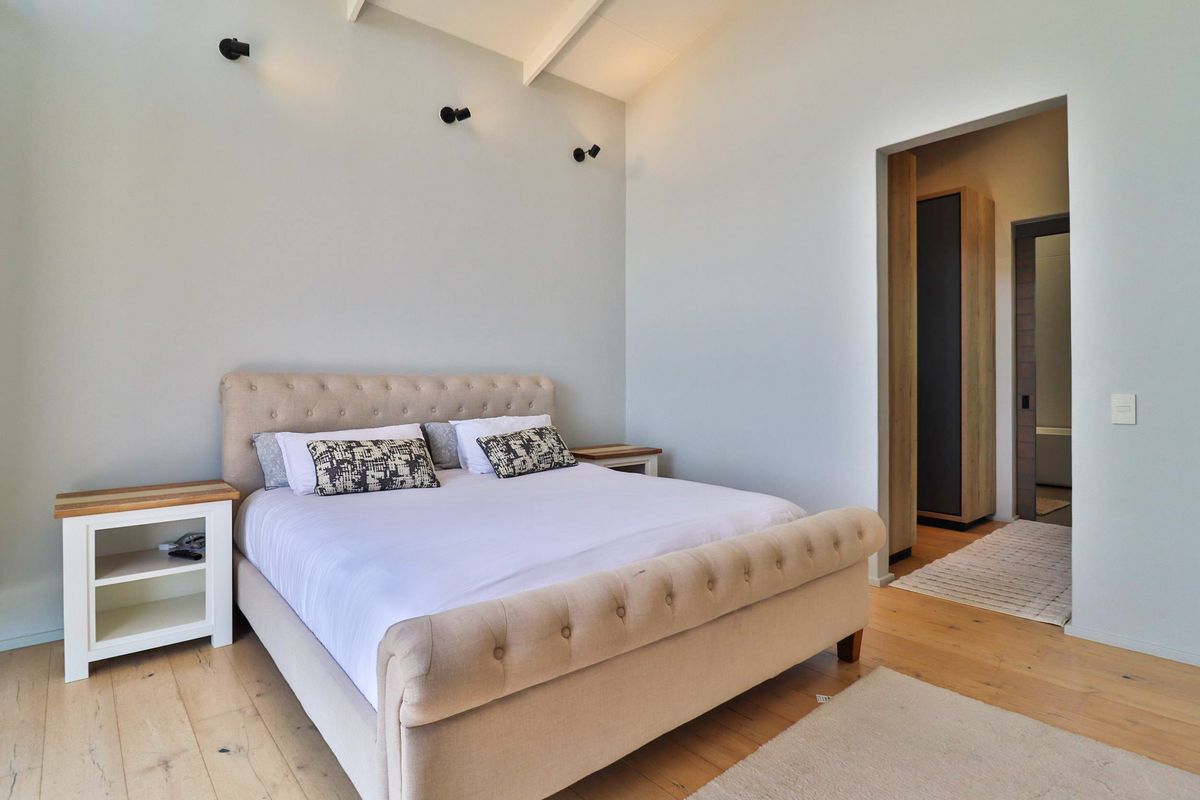 A bright, modern bedroom featuring vaulted ceilings with exposed rafters, hardwood flooring, and an adjoining walk-in wardrobe area.