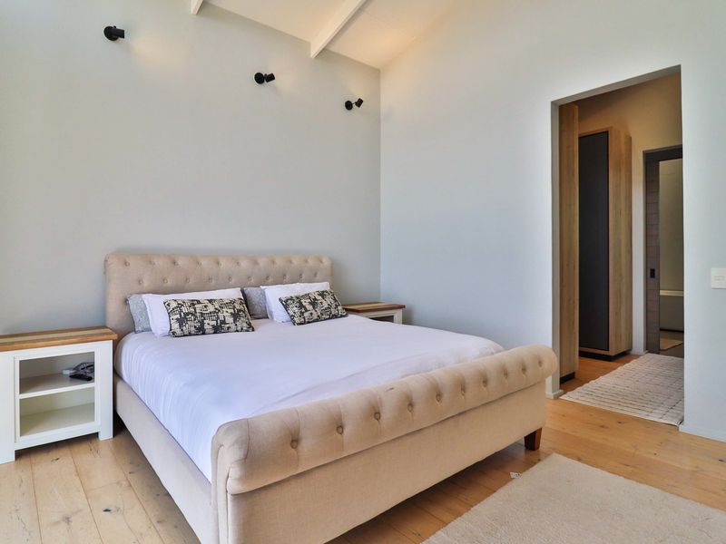 A bright, modern bedroom featuring vaulted ceilings with exposed rafters, hardwood flooring, and an adjoining walk-in wardrobe area.