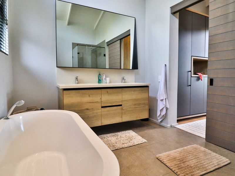 Modern bathroom featuring a double vanity with wood-finish cabinetry, a large wall mirror, a freestanding bathtub, and sleek tiled flooring.