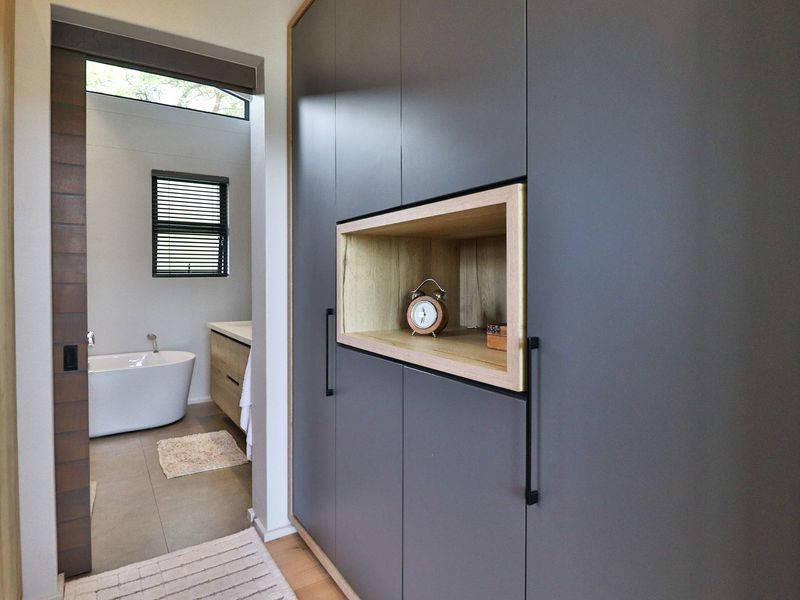 A modern hallway featuring sleek built-in cabinetry with integrated shelving, leading into a contemporary bathroom with a freestanding tub.