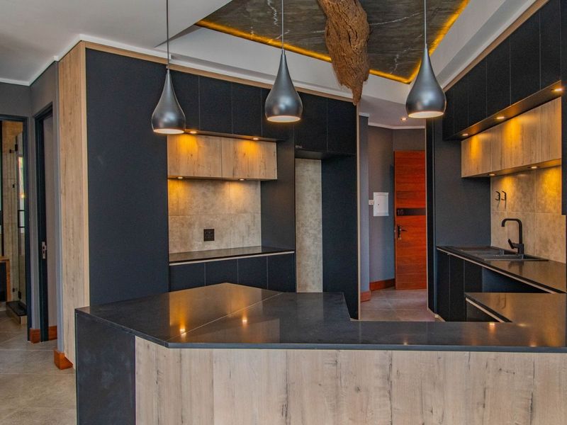 Modern kitchen featuring sleek dark cabinetry, wood-grain accents, stone countertops, and integrated lighting, offering a contemporary and functional culinary space.