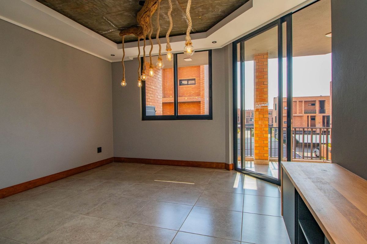 Modern living area featuring tiled floors, exposed concrete ceiling, and large sliding glass doors opening onto a private balcony.