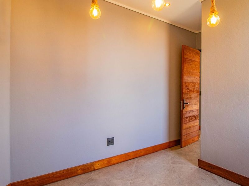 A bright, empty bedroom featuring neutral walls, tiled flooring, wooden skirting boards, and modern pendant lighting.