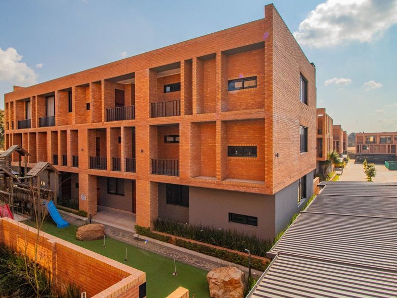 A modern multi-story apartment complex featuring exposed brick architecture, private balconies, and well-maintained communal outdoor spaces with paved walkways.