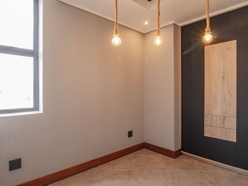 A modern, empty bedroom featuring sleek built-in cupboards, tiled flooring, and stylish pendant lighting, offering a clean and contemporary space ready for furnishing.