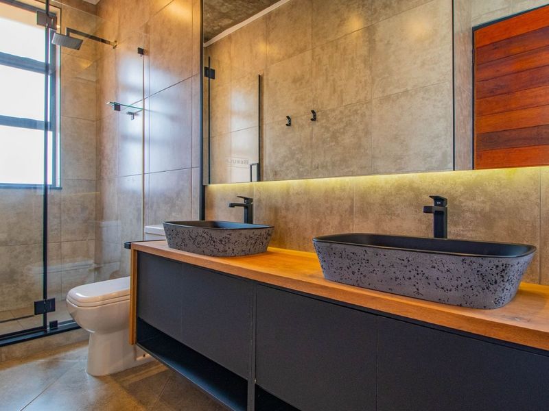 Modern bathroom featuring a double vanity with stone vessel sinks, a walk-in shower with glass screen, and contemporary tiled finishes.