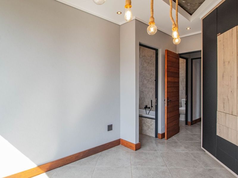Modern bedroom featuring tiled flooring, built-in cupboards, and recessed lighting, with an adjoining bathroom visible through the doorway.