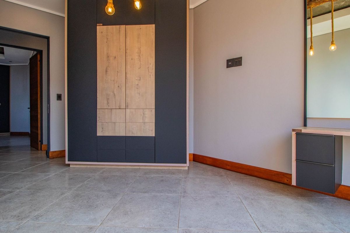 A modern, empty bedroom featuring sleek built-in wardrobes, a matching vanity unit, and neutral tiled flooring with timber skirting boards.