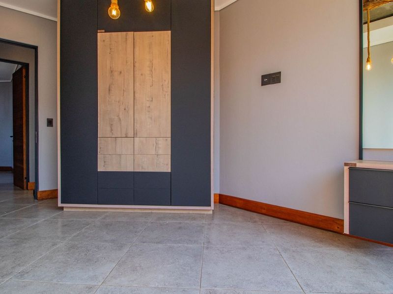 A modern, empty bedroom featuring sleek built-in wardrobes, a matching vanity unit, and neutral tiled flooring with timber skirting boards.