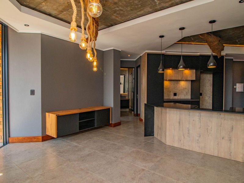 Modern open-plan living and kitchen area featuring exposed concrete ceilings, sleek cabinetry, stone countertops, and large sliding doors leading to an outdoor space.