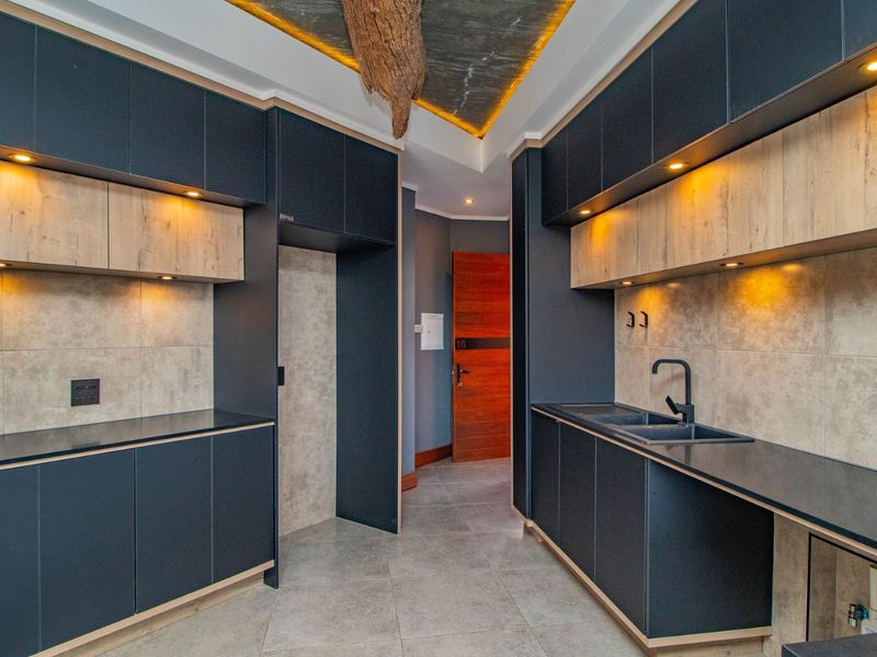 Modern kitchen featuring dark matte cabinetry, light wood accents, stone countertops, integrated appliance spaces, and contemporary recessed lighting.