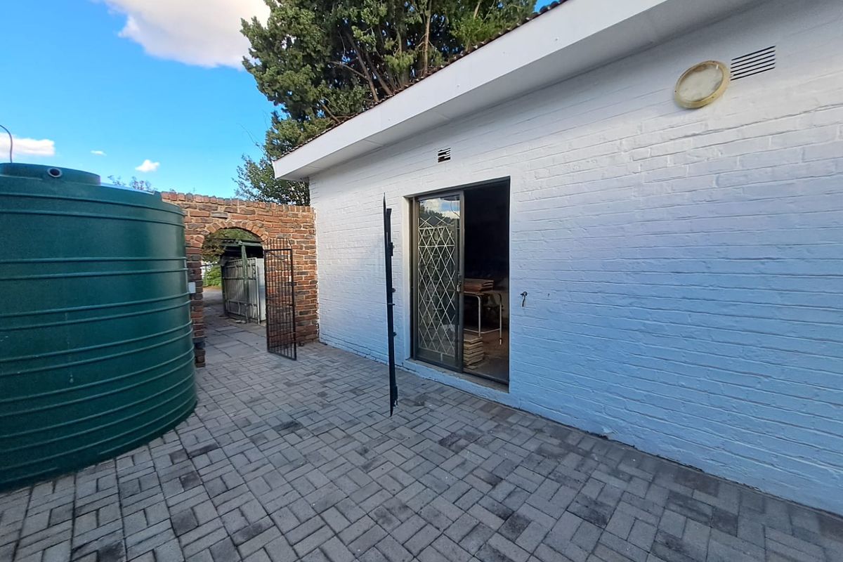 Rear exterior view featuring a paved patio area, a large water storage tank, and a sliding glass door entrance with a security gate.