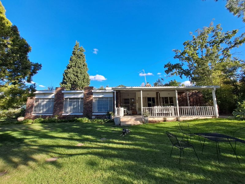 Rear view of a single-story brick house featuring a covered patio area overlooking a spacious green lawn.