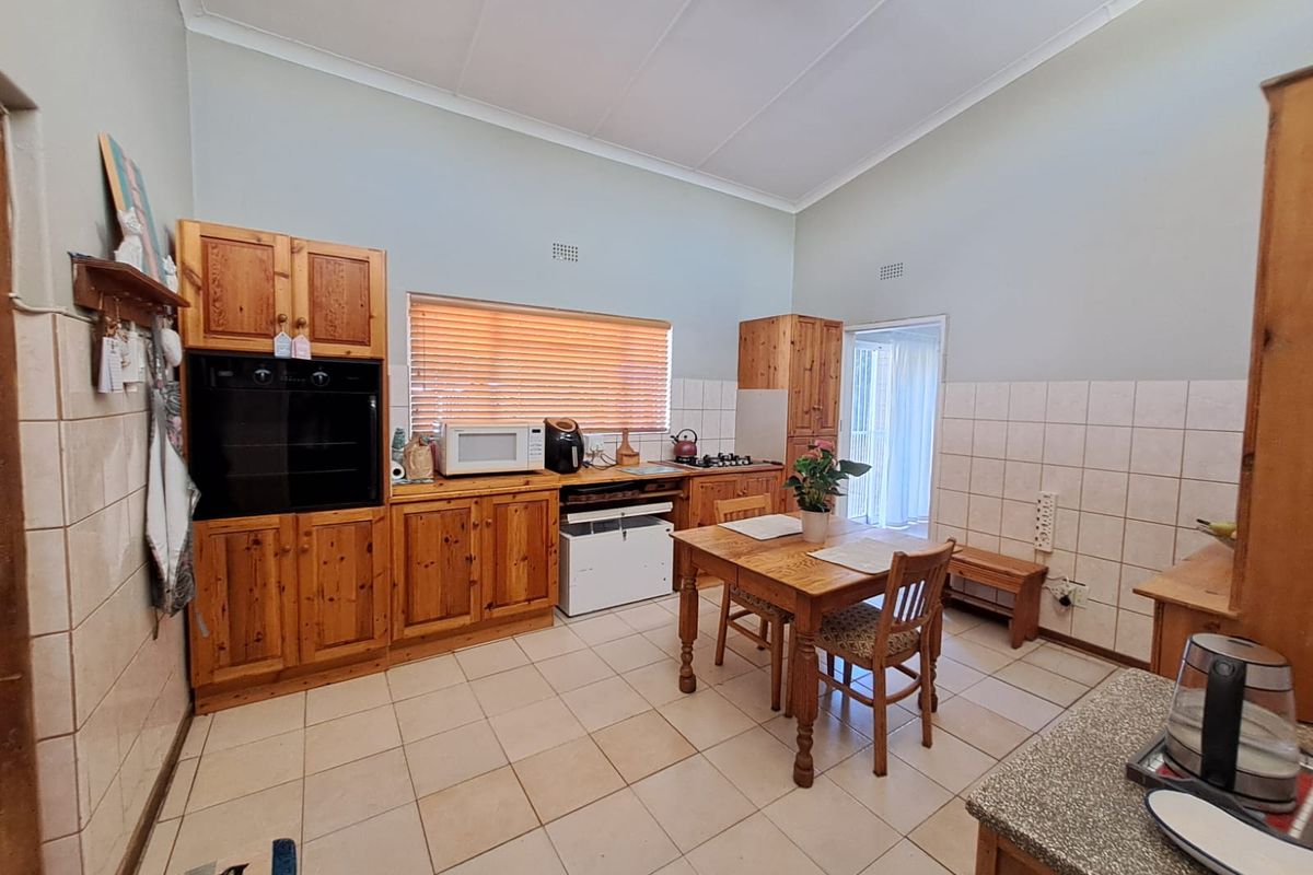 A functional kitchen featuring built-in wooden cabinetry, tiled flooring, and a tiled splashback, offering a traditional layout with integrated cooking appliances.